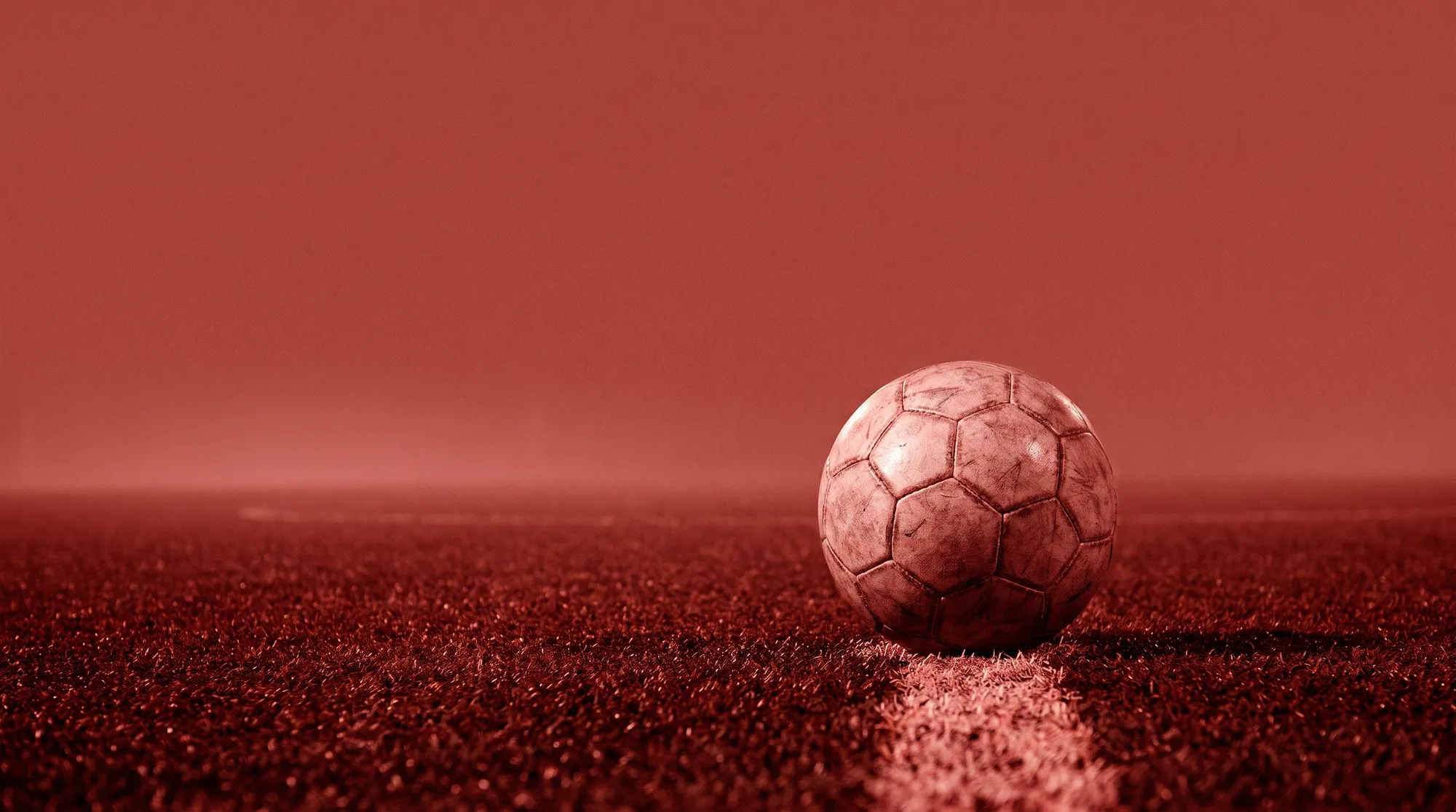 Ein Fußball liegt im roten Flutlicht auf einer Linie im Kunstrasen