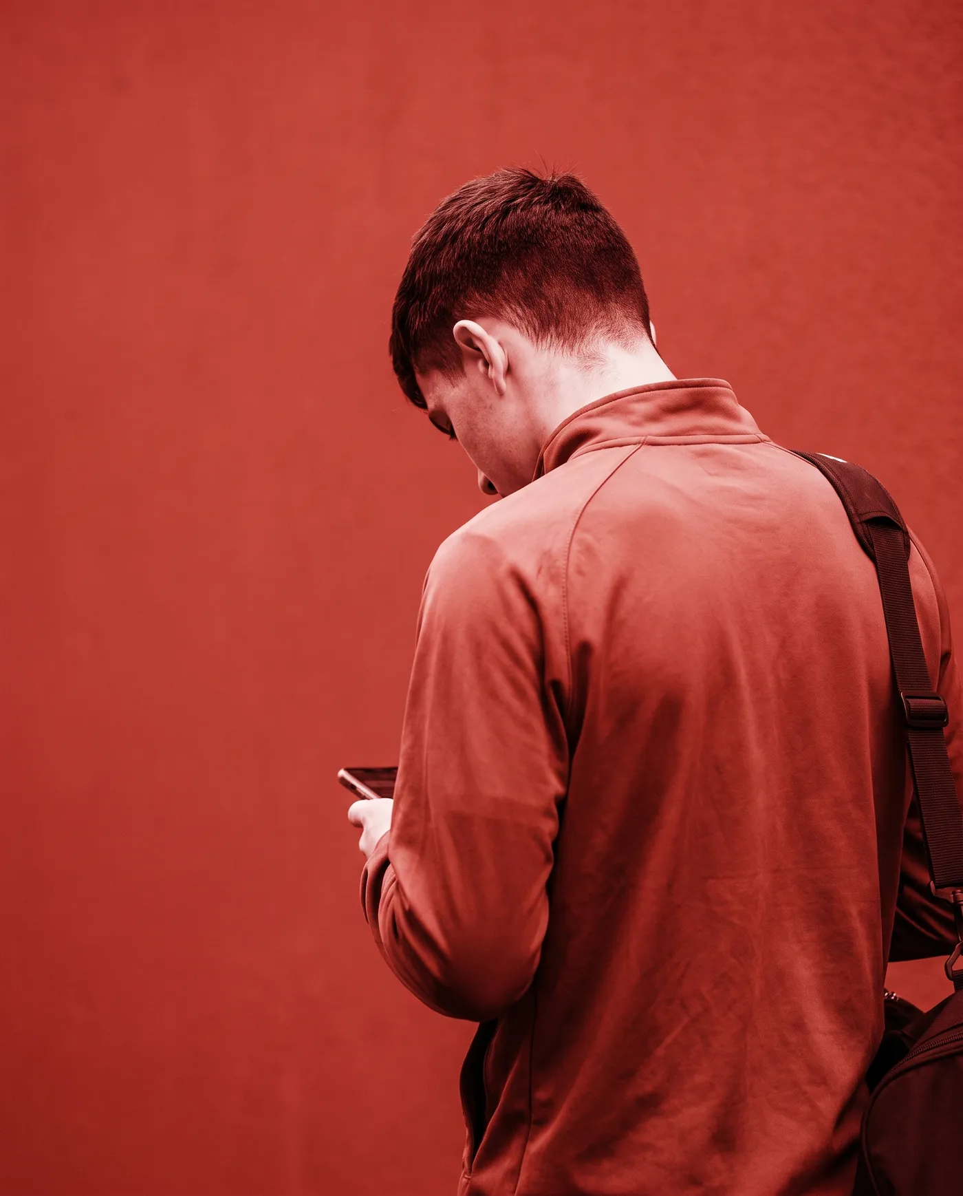 Ein Spieler in Trainingsjacke schaut auf sein Handy, von hinten fotografiert